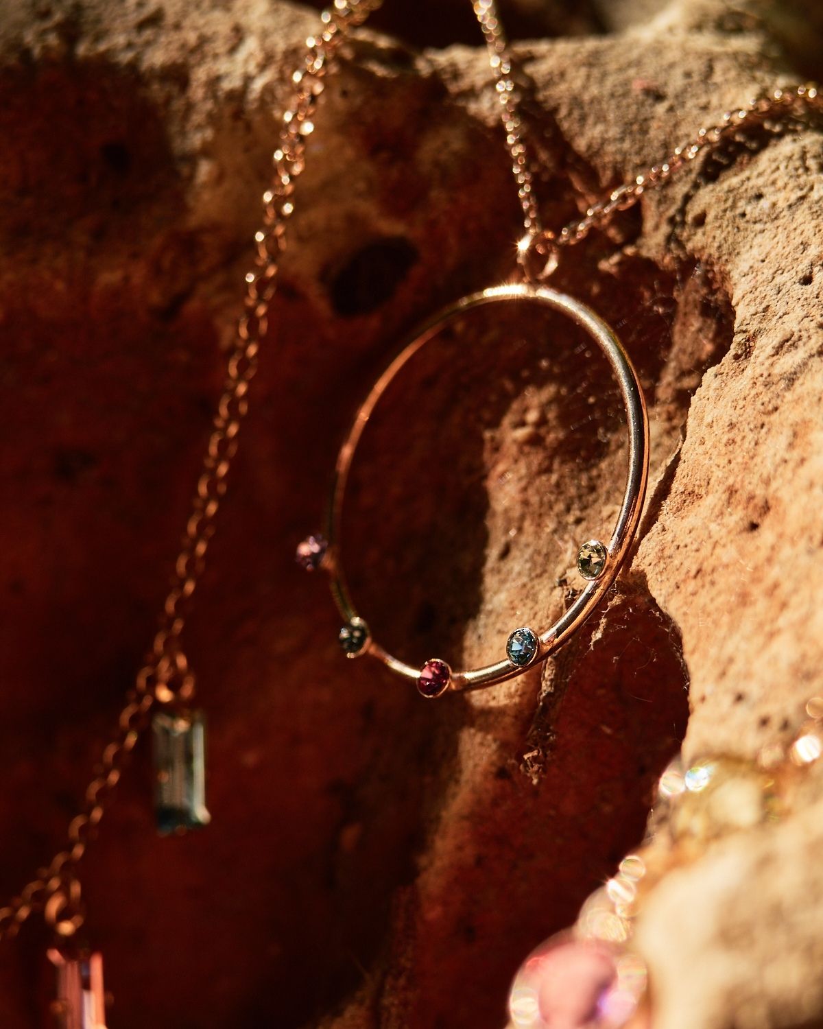 Round Necklace Multicolor Crystals-Rose Gold Close-up of a round rose gold necklace with multicolor crystals, displayed against a rustic rock background